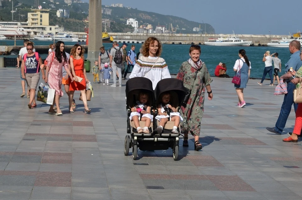 Мама с коляской на ровной набережной Ялты, море и пальмы на заднем плане